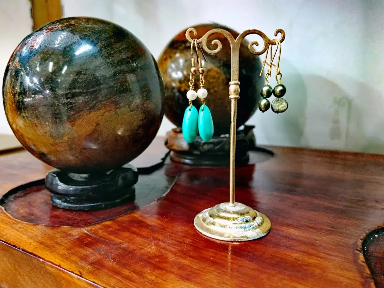 Boucles d'oreilles turquoise et perles sur support doré devant des sphères de pierre