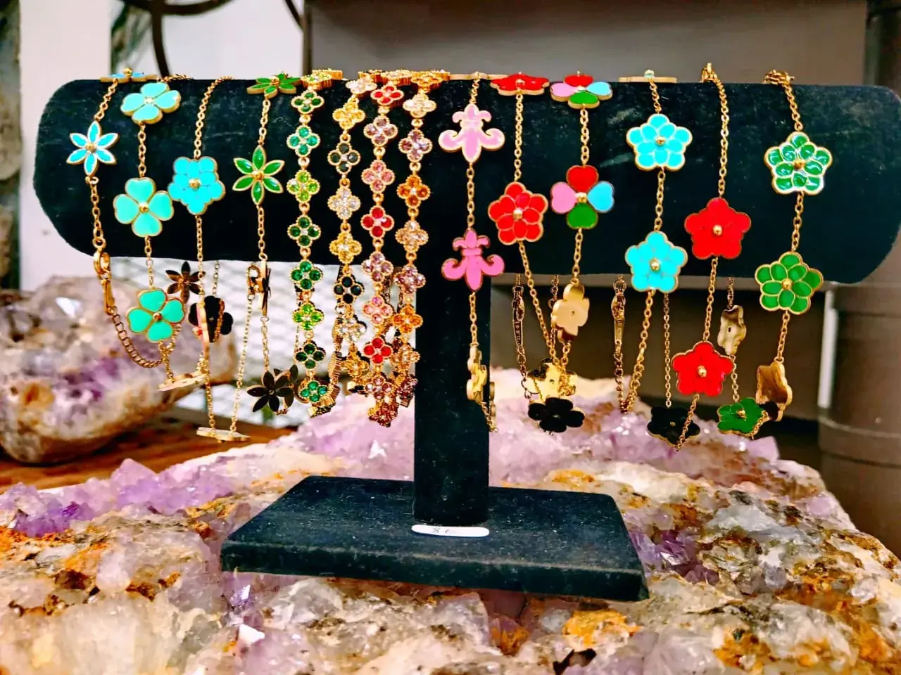 Bracelets dorés à fleurs et trèfles émaillés colorés sur présentoir, posés sur de l'améthyste